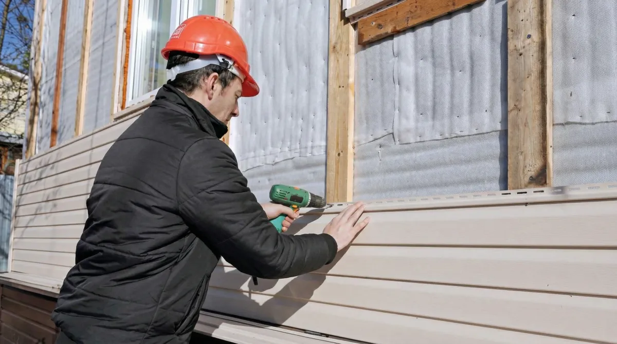 Siding replacement professional using a power drill to install new tan vinyl siding on a home exterior in Evansville, IN